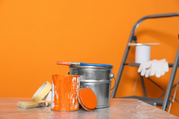 Wall Mural - Can with paint, brush and renovation equipment on table against orange background