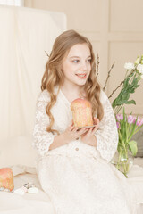 Wall Mural - A girl with long hair in a light dress is sitting at the Easter table with cakes, spring flowers and quail eggs. Happy Easter celebration.