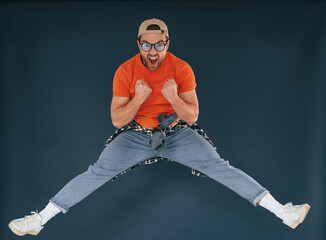 Wall Mural - Jumping, feeling good, excited. Handsome man is in the studio against blue background