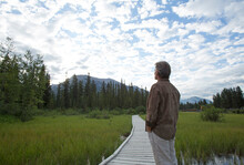 Man Stands On Boardwalk, Mountains Distant