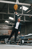 Fototapeta Tulipany - Having fun by hanging on the crane's hook. Manager in black formal wear at the factory