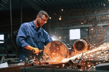 Wall Mural - Welding the metal. Factory worker in blue uniform is indoors