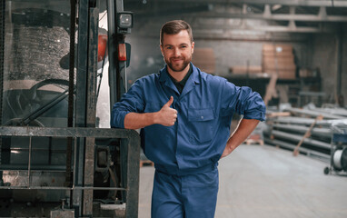 Wall Mural - Leaning on the forklift. Factory worker in blue uniform is indoors