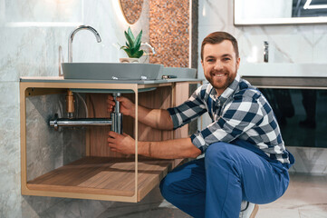 Wall Mural - Positive plumber in blue uniform is at work in the bathroom