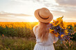 © maryviolet - Back view of woman enjoying view in blooming sunflower field at sunset with bouquet of flowers. Peace and freedom
