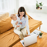 Fototapeta  - Smiling happy young mother with newborn baby working in online conference mode