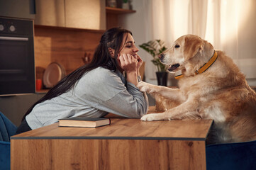 Sitting by the table together. Woman is with golden retriever dog at home