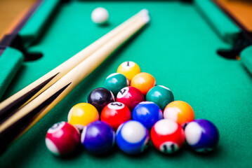 Billiard cues and pyramid of multicolored snooker pool balls on green billiard table.