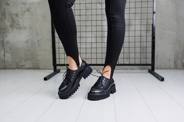 Female legs in trendy black leggings and loafers, laces on leather shoes, details of a stylish autumn fashion look