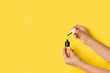Manos de mujer sosteniendo un esmalte de uñas de color negro sobre un fondo amarillo brillante liso y aislado. Vista de frente y de cerca. Copy space
