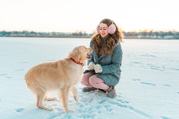 Wall Mural - Big golden retriever dog giving a paw its owner on a background of winter ice river. Winter white landscape. Sunny weather. Friendship, pet and human.