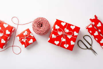 Wall Mural - Valentine's Day concept. Top view photo of present boxes wrapping paper rolls spool of twine and scissors on isolated white background