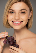 happy young woman holding fresh grapes and smiling isolated on grey.