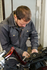 Poster - The mechanic connects the electrical cables of the motorcycle. Vertical frame.