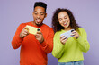 © ViDi Studio - Young couple two friends family man woman of African American ethnicity wear casual clothes together use play racing app on mobile cell phone gadget isolated on pastel plain light purple background.