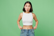 Young amazed surprised woman wear white clothes show loose pants on waist after weightloss isolated on plain pastel light green background. Proper nutrition healthy fast food unhealthy choice concept.