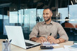 © Liubomir - Successful african american businessman inside office doing paperwork, man writing information, worker using laptop for work sitting with bills and contracts smiling and satisfied with result.