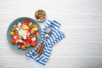 greek fresh healthy colorful salad with feta cheese, vegetables, olives in blue bowl on rustic white