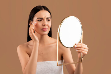 Stressed half-naked woman looking at mirror and touching her face