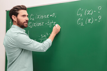 Mature teacher explaining mathematics at chalkboard in classroom