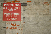 Old Parking By Permit Only Violators Will Be Towed Sign On Brick Wall