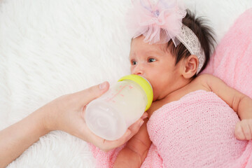 Wall Mural - mother feeding milk bottle to her newborn baby girl on bed