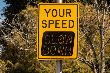 Yellow digital sign measuring traffic speed. The sign says Your Speed  and shows Slow Down in digital letters