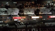 Red Big Trucks With Coca Cola Drive Through The Streets Of The City. Average Traffic Of Cars. Lights And Headlights Are Shining. New Year's Mood. Top View From The Drone On The Houses And The Road