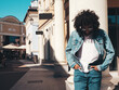 © halayalex - Handsome confident hipster model. Sexy unshaven Arabian man dressed in summer jeans jacket clothes. Fashion male with long curly hairstyle posing in street at sunset. Cheerful and happy. In sunglasses