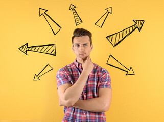 Choice in profession or other areas of life, concept. Making decision, thoughtful young man surrounded by drawn arrows on yellow background