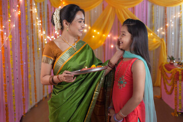 Young Indian mother and daughter during puja at home - Diwali / Durga Puja. A cute little girl in Indian clothes - salwar and kameez with her mother who is holding puja Thali. Indian customs during...