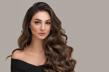 Portrait of a beautiful young woman with long curly hair. Grey background