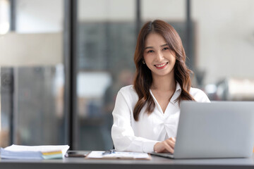 Wall Mural - Charming Asian woman working at the office using a laptop Looking at the camera.