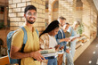 © K.A./peopleimages.com - University, hallway and portrait of Indian man and students standing in row together with books at business school. Friends, education and future, happy man in study group on campus in lobby for exam