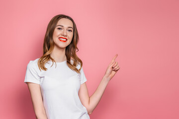 girl with in a white t-shirt smiles and points her finger at copy space