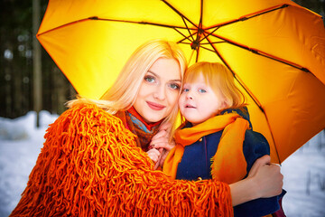 Wall Mural - Family with daughter and mother in orange dress with yellow umbrella having fun and joy in woods, forest or park with snow at winter day