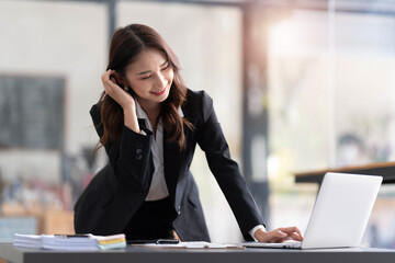 Wall Mural - Focused young businesswoman standing at table in office, using laptop, looking at computer screen, reading or writing business email, searching information in internet, working on project