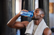 Drinking water, fitness and gym with a black man athlete taking a break from his exercise or workout routine. Training, health and wellness with a sporty male having a drink for hydration or recovery