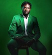 © Lou W/peopleimages.com - Fashion, formal and portrait of a black man in a suit sitting on a chair in studio with a luxury outfit. Elegant, stylish and African male model with fashionable clothes isolated by green background.