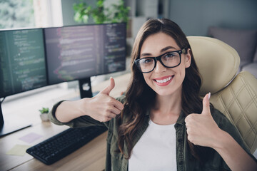 Photo of happy cheerful lady content maker wear glasses smilig showing two thumbs up indoors workstation workshop