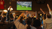 Group Of Soccer Fans Cheering, Screaming, Raising Hands And Jumping During A Football Game Live Broadcast In A Sports Pub. Player In Blue Shirt Scores A Goal And Friends Celebrate. Slow Motion Footage