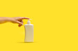 Mano de mujer apretando un bote dispensador de plástico blanco sobre un fondo amarillo brillante liso y asilado. Vista de frente y de cerca. Copy space