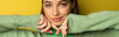 Pretty teenage girl in green jumper looking at camera on yellow background, banner.