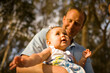 © Cavan Images - A baby girl looks up with wonder while being held on her father's lap, outdoors on a sunny day in California.