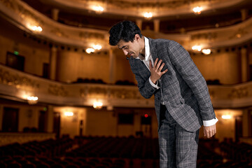 man Presenter in elegant classic suit on Stage is expressing gratitude to audience after performance, bow down, handsome american or european guy after successful presentation, skilled and talented