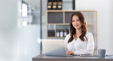 Wall Mural - Charming Asian woman working at the office using a laptop Looking at the camera.