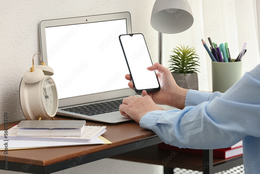 Woman working with modern laptop and mobile phone at table in office