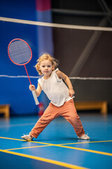 Little girl three years old playing badminton in sport wear on indoor court 