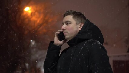 A young man speaks on the phone under snowfall