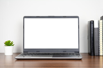Home workplace with blank transparent screen laptop and books on wooden table with white wall background